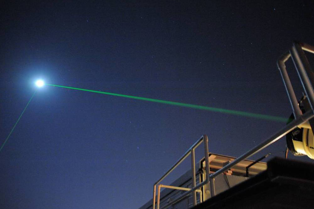 Satellite Laser Ranging station emitting green laser beam at night sky
